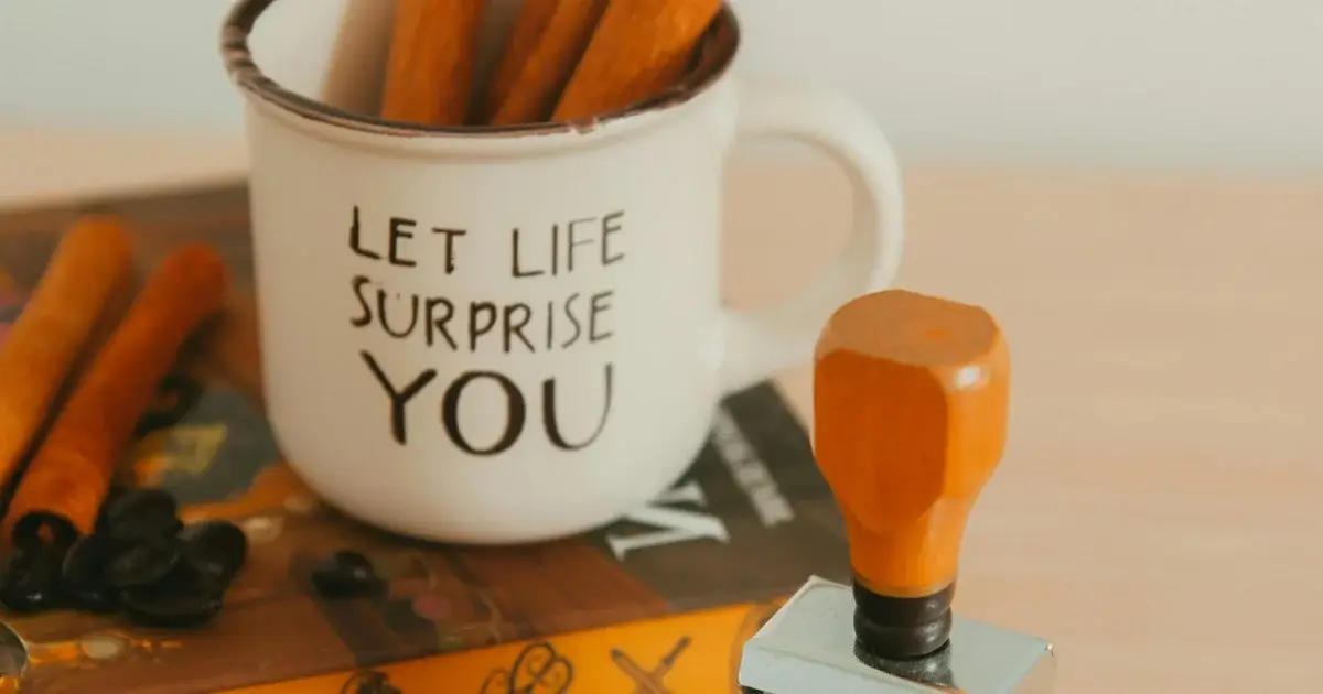 A book and a coffee on a table with a meaningful sentence `let life surprise you`.