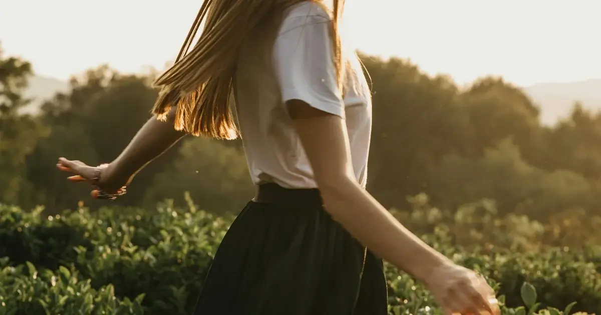 A woman walking away in tall grass and sunset.